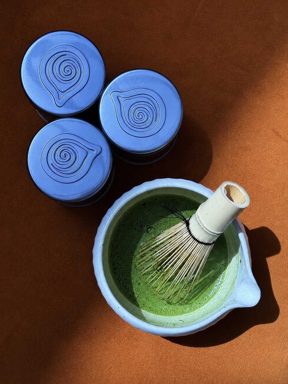 Freshly whisked Memento matcha beside three sealed tins